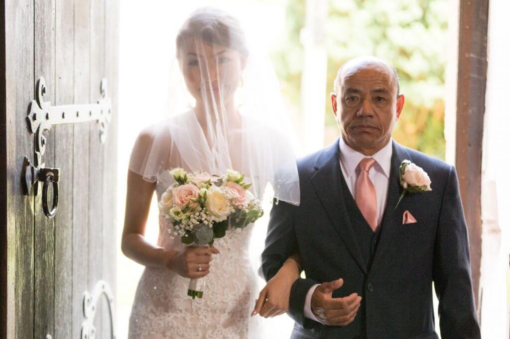 veiled bride walks down aisle with father carrying floral bouquet iffley village church oxford oxfordshire wedding photography 07
