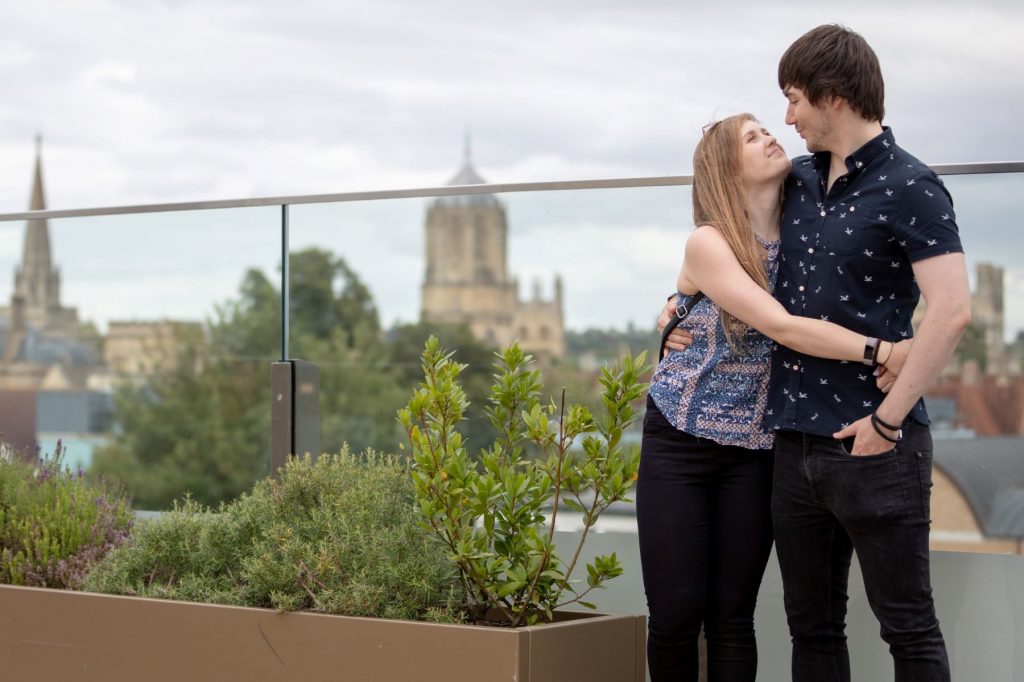couple embrace dreaming spires background oxford city centre engagement photo shoot oxfordshire wedding photographers