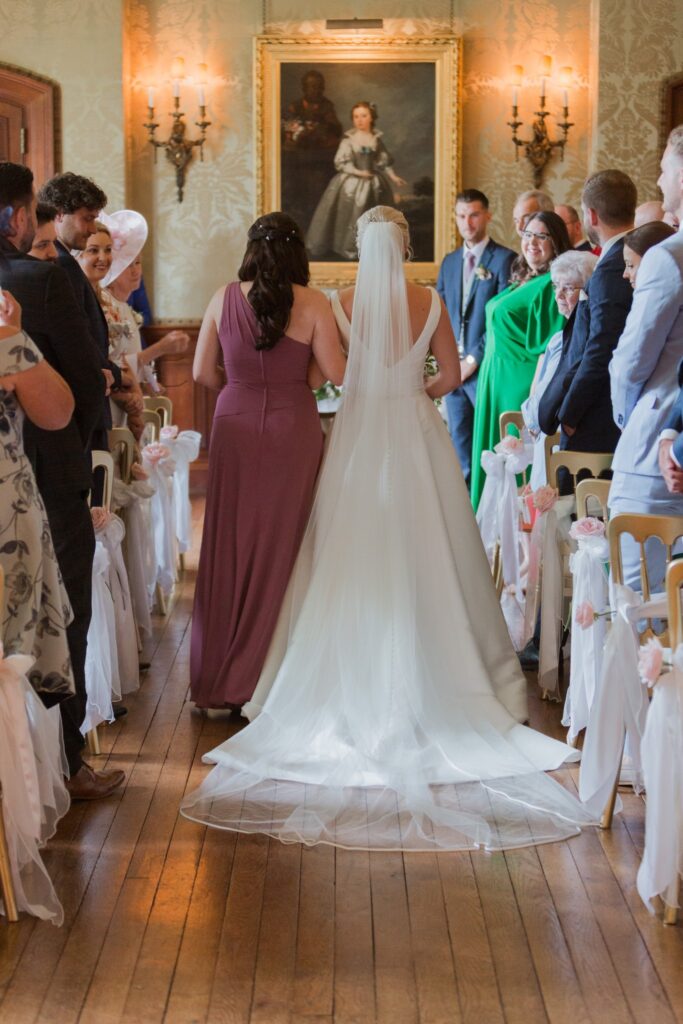 elegant bride with bridesmaid escorted down aisle holdenby northamptonshire oxford wedding photographer